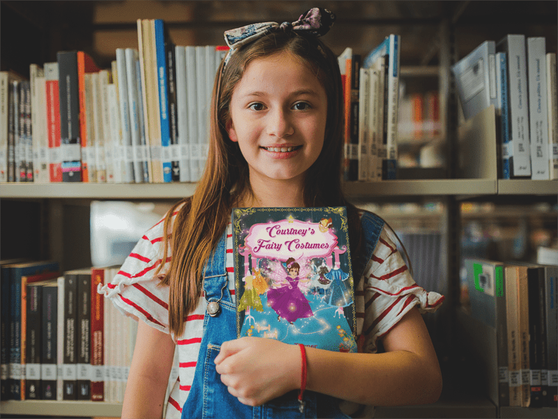 happy-little-girl-holding-a-book-mockup-at-the-library-a19273-min-min